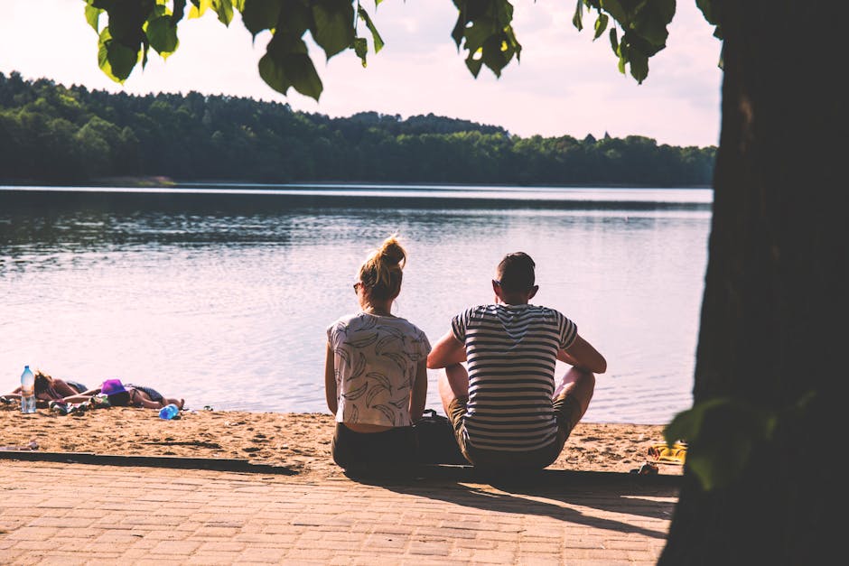 Woman in White Crop Top Besides Man in White and Black Stripes Shirt Beside Body Of Water