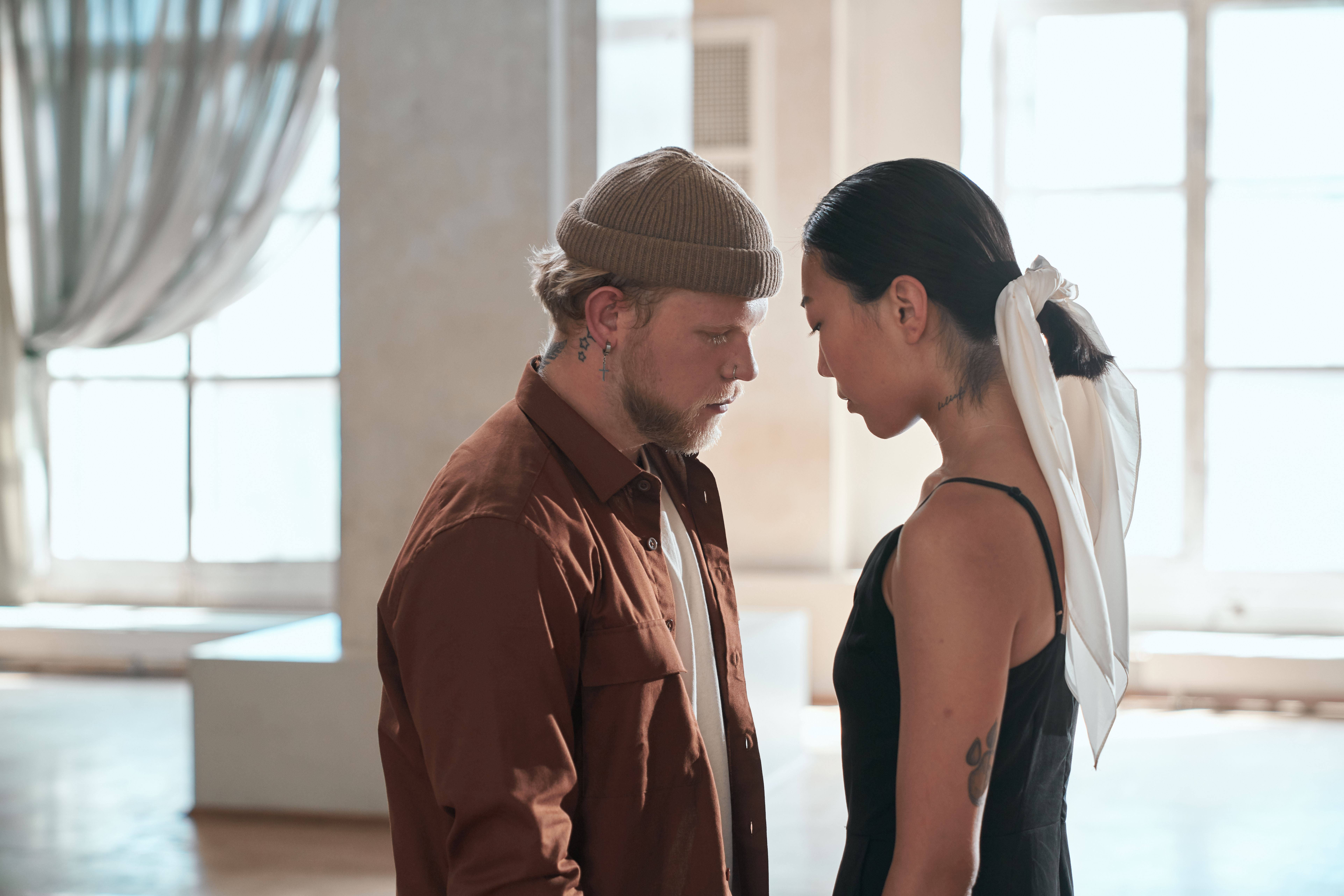 A man and woman stand face to face indoors, exuding confrontation and connection.