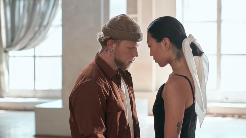 A man and woman stand face to face indoors, exuding confrontation and connection.