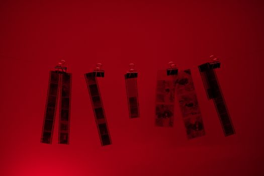 Hanging film strips illuminated by red darkroom light during development.