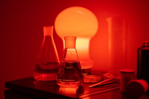 Laboratory flasks and equipment illuminated by moody red light, creating a dramatic effect.