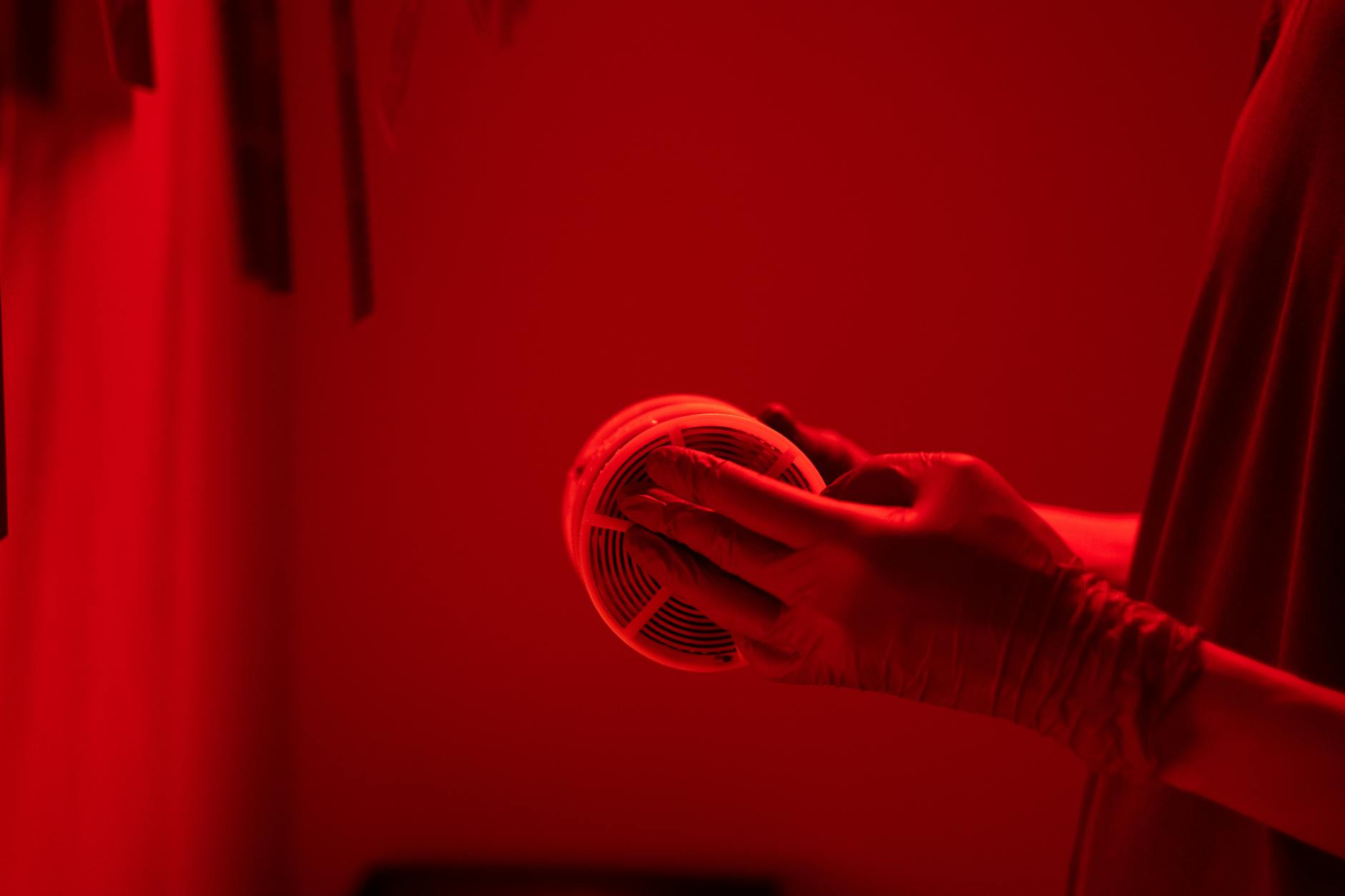 Hands in gloves handling film reel in a red-lit darkroom, essential for analog photography.