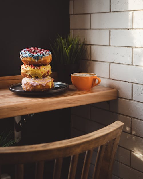 Pile of Iced Donuts on Plate and Cup of Coffee Served on Wooden Table at Cafe