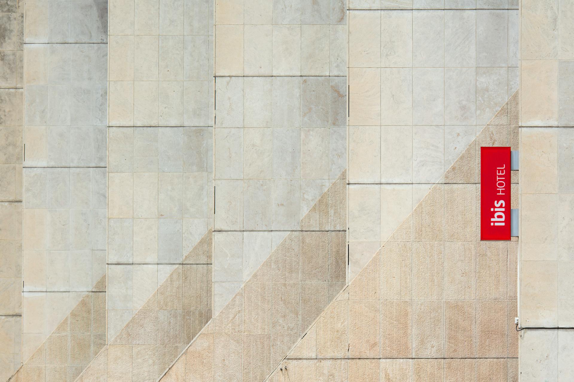 Minimalist hotel exterior with Ibis logo on a textured wall in Montpellier, France.