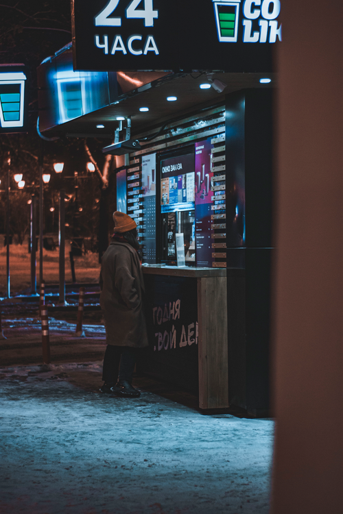 Free Person at a 24-hour coffee kiosk in an urban setting during night. Stock Photo