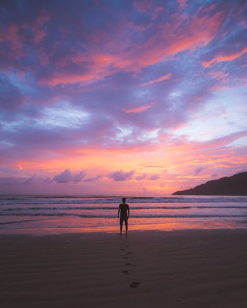 Photo of a Man Standing at the Beach During Sunrise