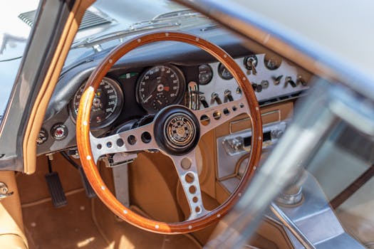 Close-up of vintage Jaguar E-Type car interior featuring a wood steering wheel and classic dashboard design.