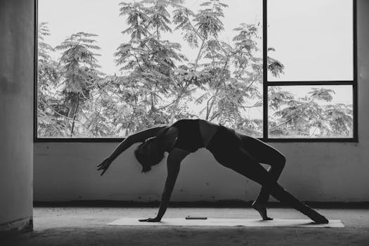 Black and white silhouette of a woman performing yoga indoors with trees visible through the window.