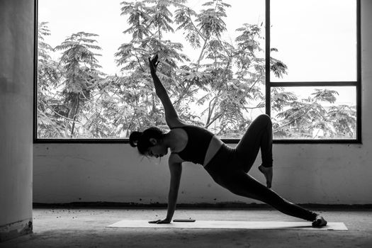 Black and white image of a woman practicing yoga indoors near a large window.