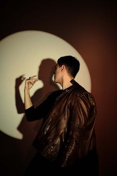 A fashionable man poses in a leather jacket, casting a striking shadow on the wall.