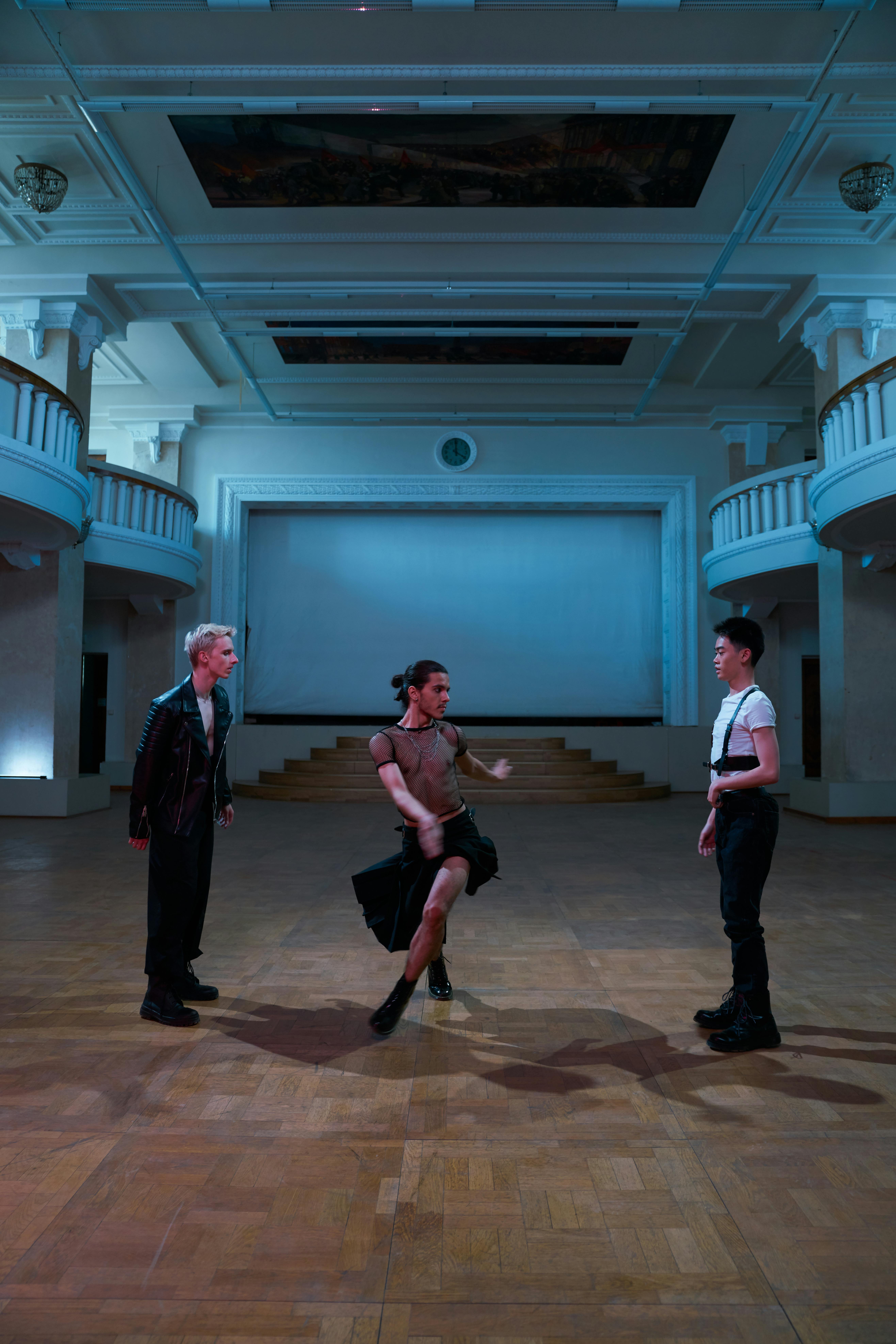 Free Three dancers perform a contemporary routine in an elegant indoor hall, showcasing movement and style. Stock Photo