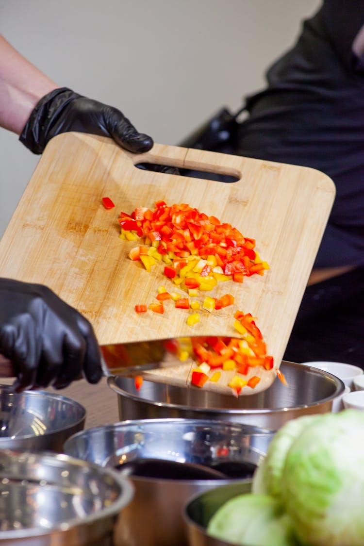 A Person Putting Chopped Bell Peppers On A Stainless Bowl