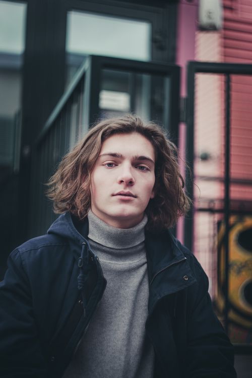 Free Young man with long hair and casual jacket in an urban setting. Stock Photo