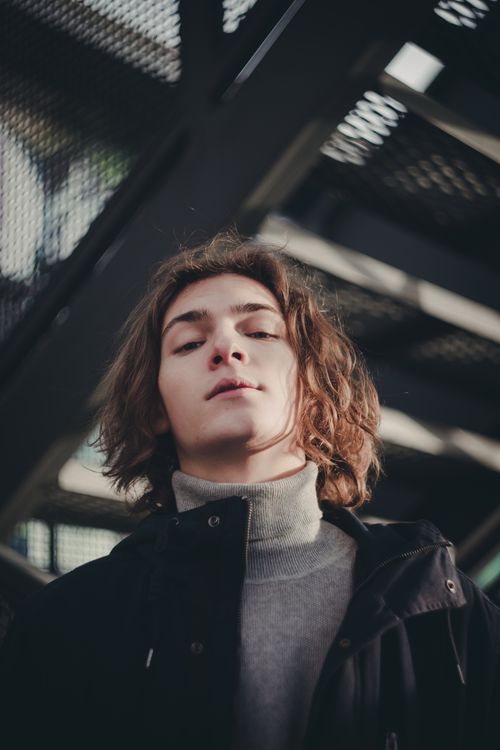 Free Young man with curly hair in a turtleneck posing stylishly outdoors, conveying modern fashion. Stock Photo