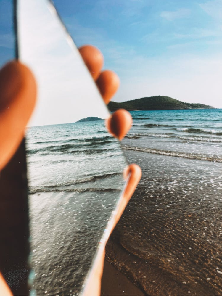 Fingers Holding Mirror On Sea Shore