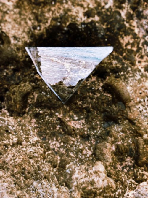 Free Close-up of a triangular mirror reflecting the ocean, placed on a textured rock surface. Stock Photo