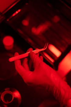 A gloved hand holding tweezers in a photography darkroom under red light.