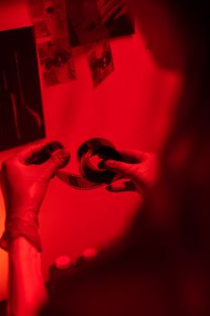 A person examining film negatives in a darkroom under red light.