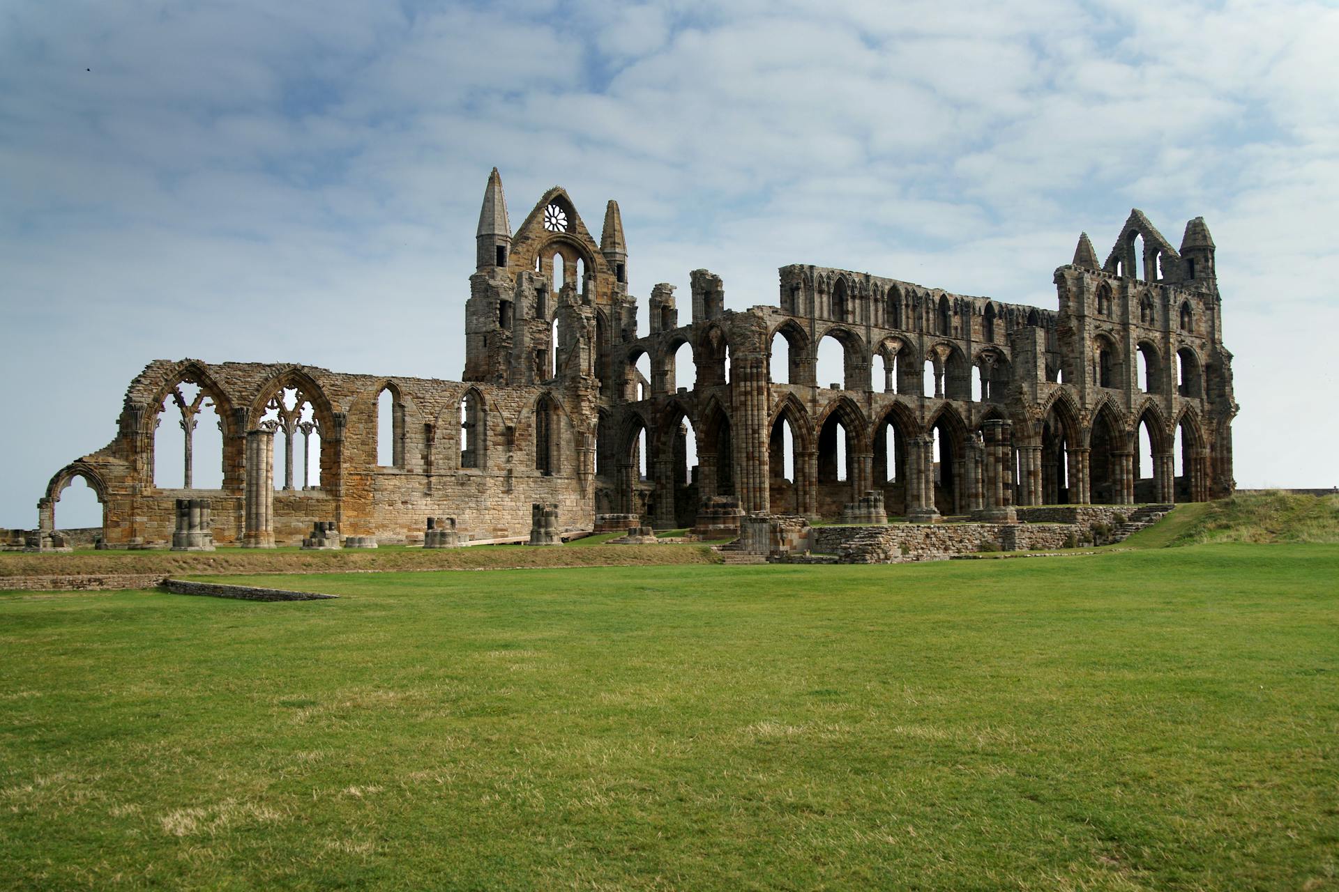 Explore the historical Gothic ruins of Whitby Abbey under a serene sky.