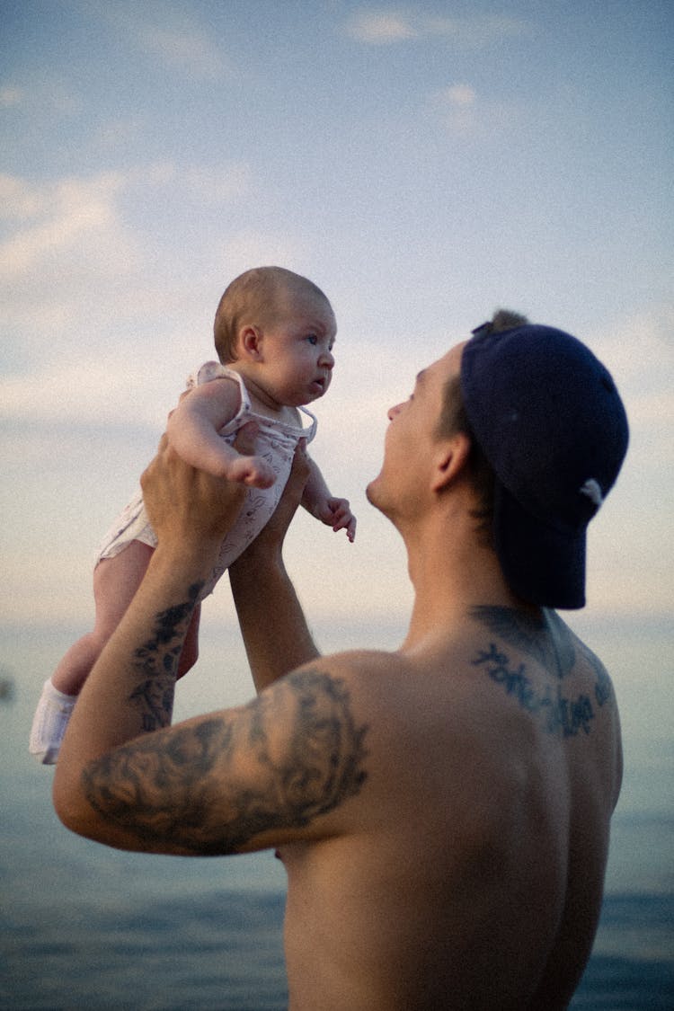 Man In Cap Standing In Water Holding Baby