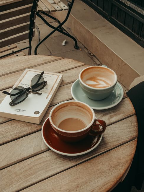 A small café table with two cups of coffee, sunglasses, and a book, creating a cozy ambiance.