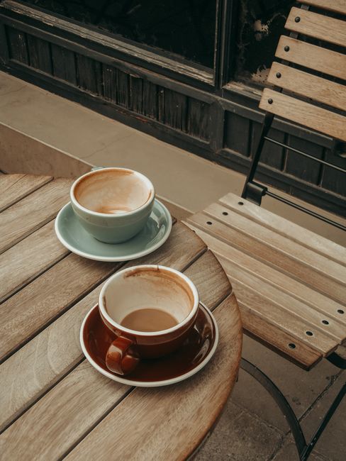 Two empty coffee cups on a rustic wooden table at an outdoor café, inviting and cozy.