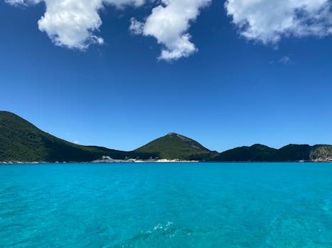 Peaceful seascape with turquoise waters and green hills under a clear blue sky.