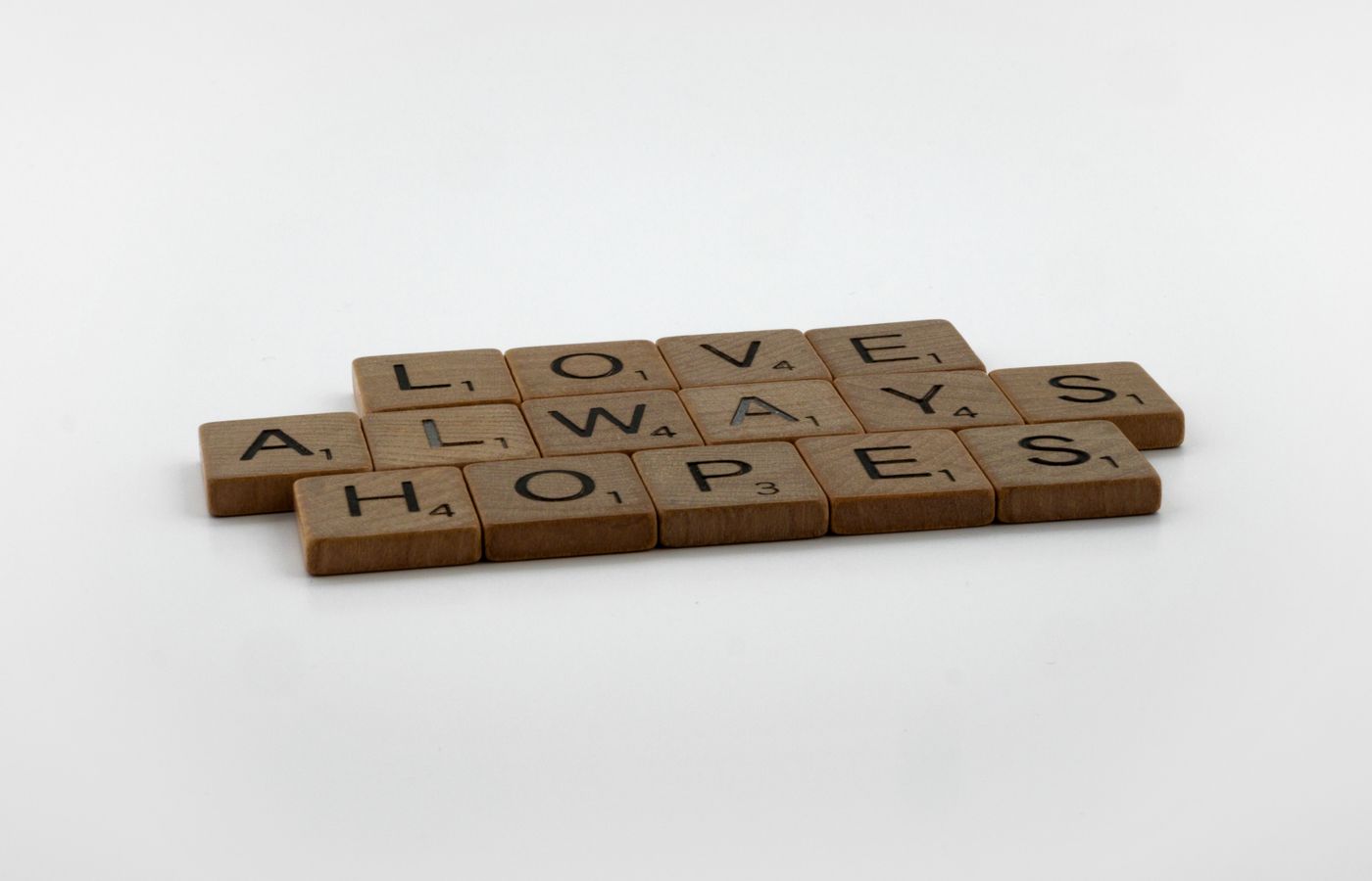 A thoughtful message spelled with Scrabble tiles on a white surface, conveying hope and love.