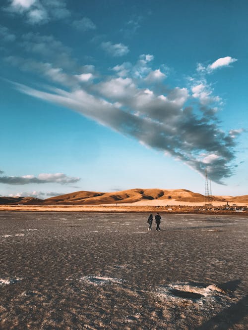 2 People Walking on Gray Sand Under Blue Sky