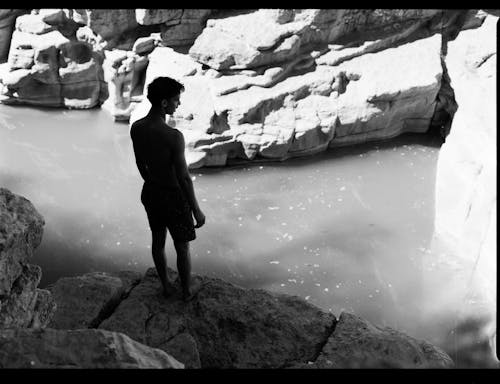 Grayscale Photo of a Man Standing on the Edge of a Cliff