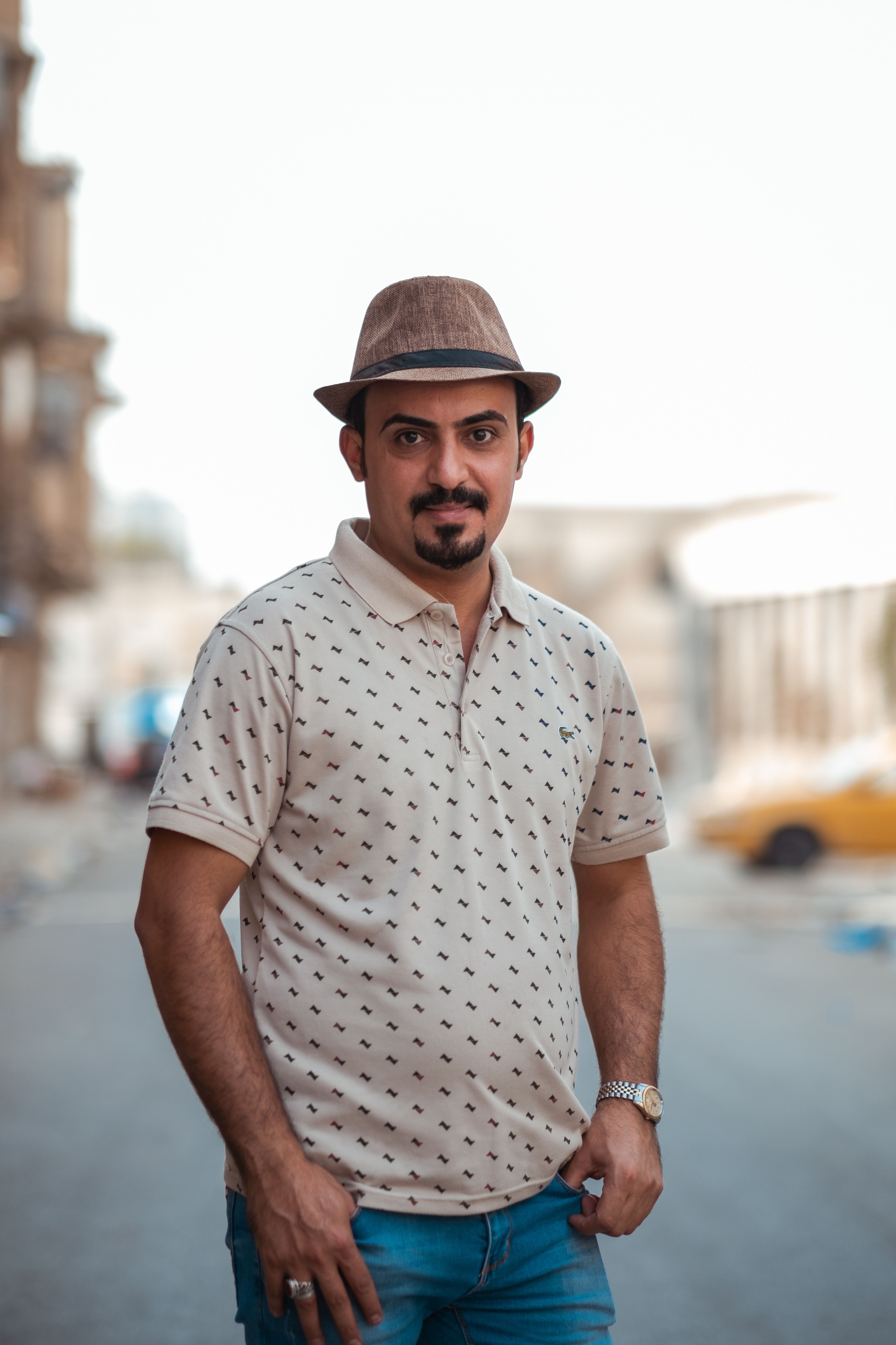 Fashionable man with mustache and hat posing confidently on a city street.