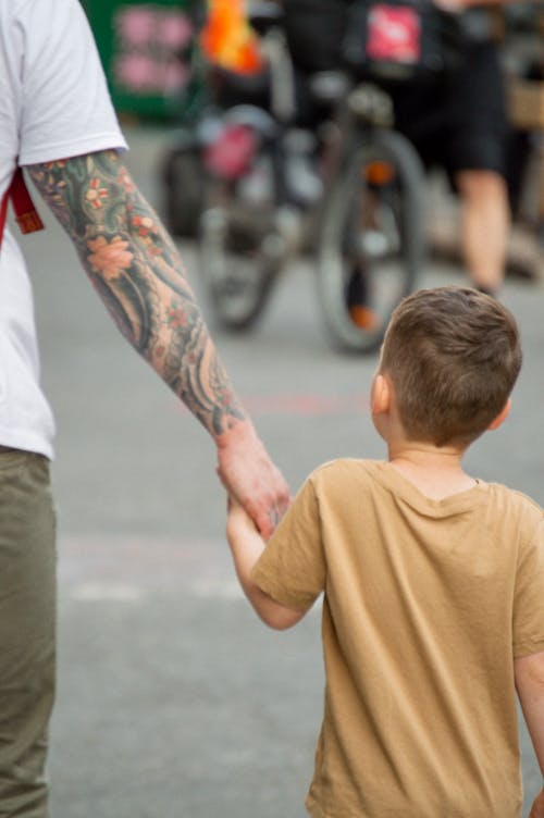 Free Person with Arm Tattoo Holding the Hand of a Boy Stock Photo