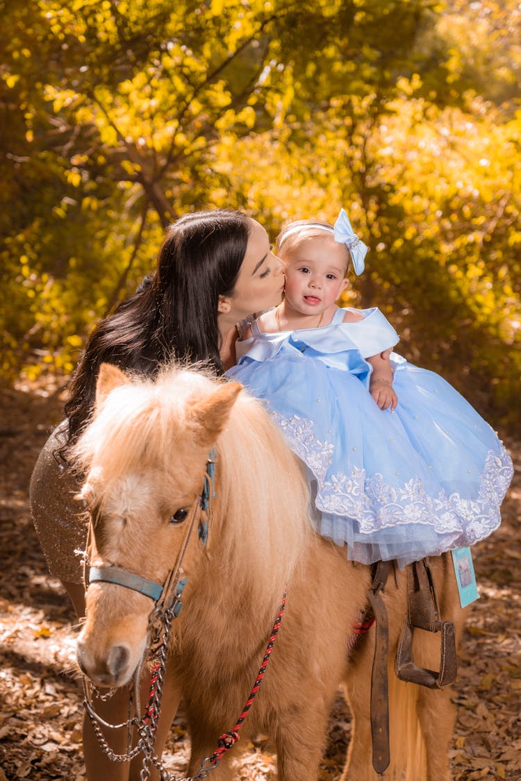 A Girl In Blue Dress Riding A  Horse Guided By Her Mom