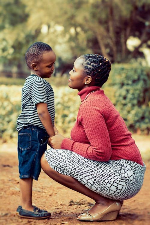 Tilt Shift Lens Photography of Woman Wearing Red Sweater and White Skirt While Holding a Boy Wearing White and Black Crew-neck Shirt and Blue Denim Short