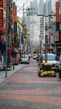 Bustling street in South Korea featuring shops, vehicles, and colorful signs.
