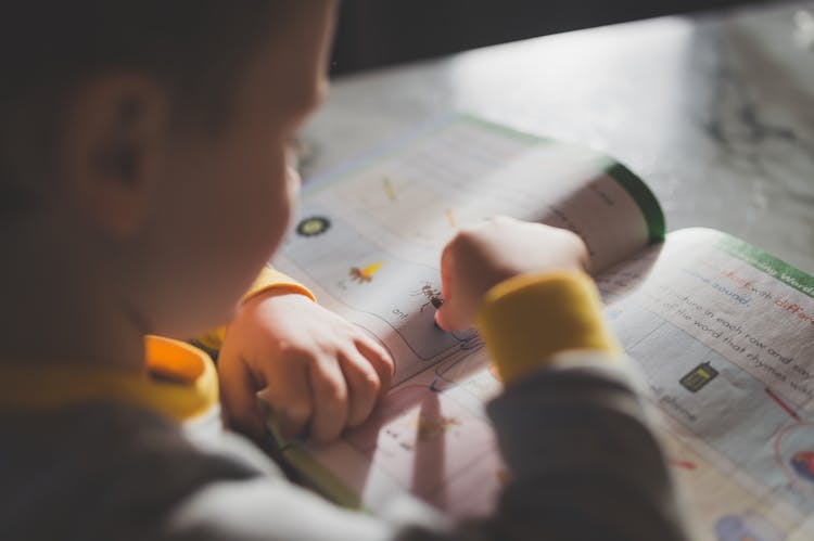 A Child Drawing On A Book Using A Crayon