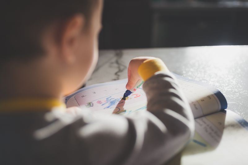 Young child engaged in a creative coloring activity with bright sunlight highlighting pages.