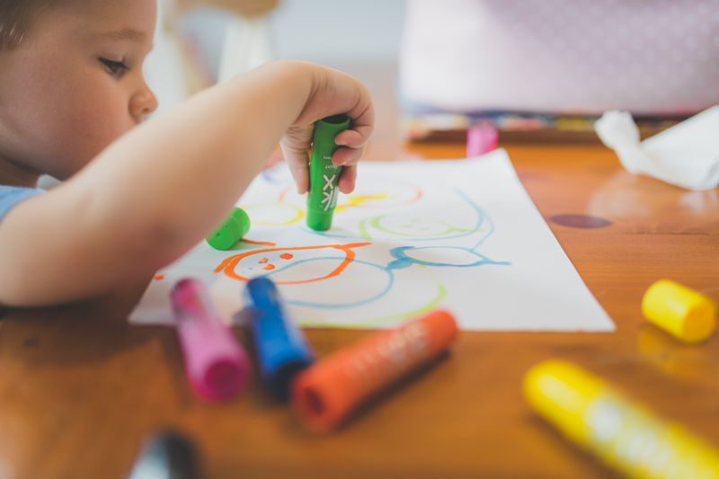 Close-up of a child drawing with vibrant markers, showcasing creativity and fun in an indoor setting.