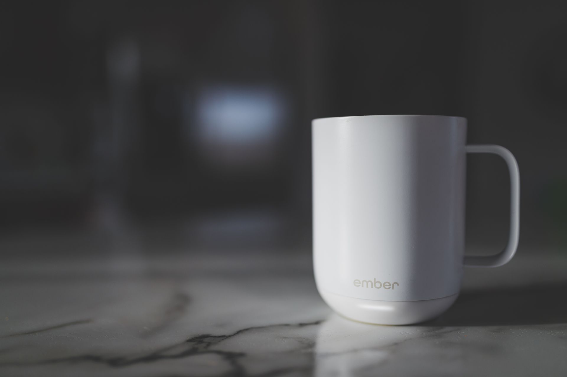 Close-up of a white Ember mug on a marble kitchen countertop with soft lighting.