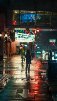 Colorful city street at night in Minneapolis with people walking and bright lights reflecting on wet pavement.