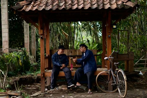 Free Two men laughing and talking on a wooden bench outdoors, with a vintage bicycle nearby. Stock Photo