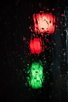 Blurred red and green traffic lights seen through rain-soaked glass at night.