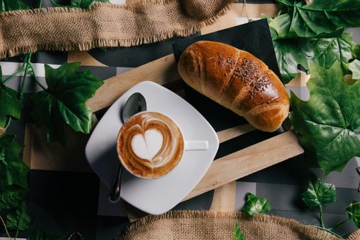 Cappuccino con latte art e cornetto su tavolo di legno