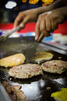 Juicy burger patties sizzling on a grill with hands flipping them close-up view.