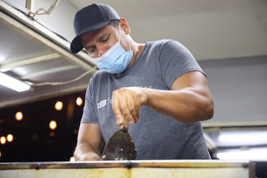 A street food vendor in a face mask prepares food during the evening at a lively market.