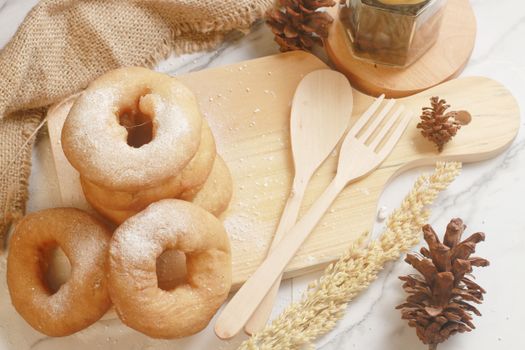 A stack of powdered donuts on a rustic wooden board with pinecones and kitchen utensils for a homely feel.