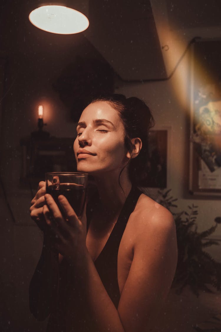 A Woman With Her Eyes Closed Smelling A Cup Of Coffee