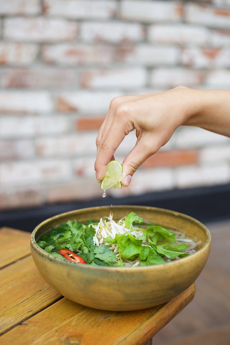 Unrecognizable Hand Squeezing Juice From Lemon Into Asian Soup