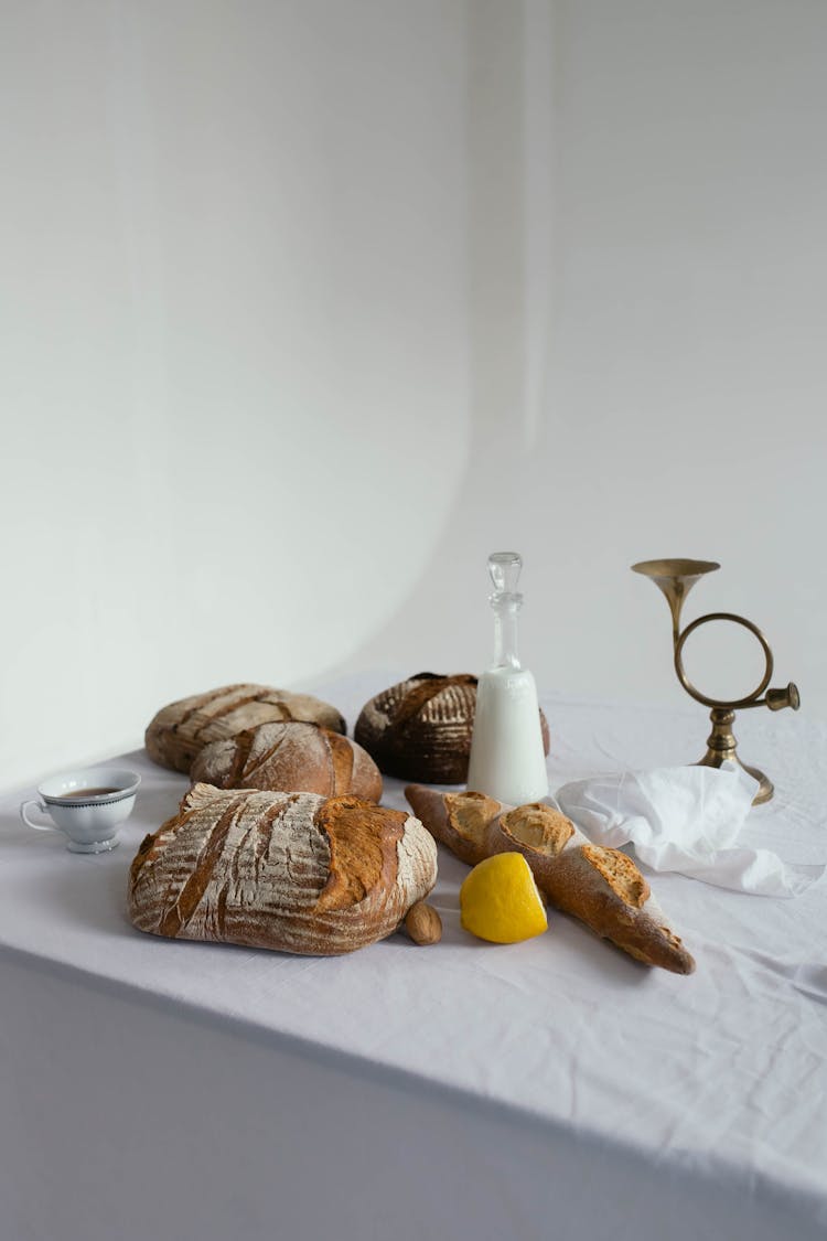 Loafs Of Bread With Carafe Of Milk And Cup Of Tea On Table