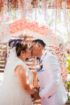 A bride and groom share a romantic kiss under a stunning floral arch on their wedding day.